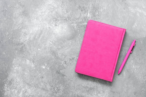 istock Pink notebook and pen on a gray concrete background. Female workspace. Top view, flat lay, copy space. 1207557825