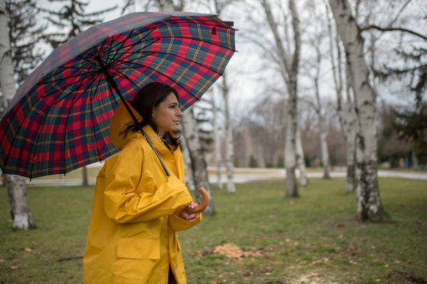 istock Young woman in yellow raincoat spending rainy day in park 1207561514