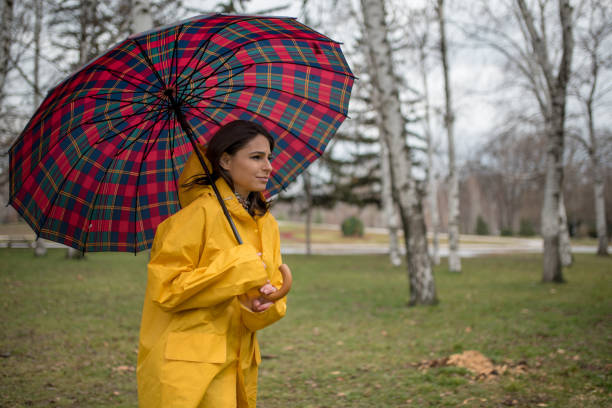 istock Young woman in yellow raincoat spending rainy day in park 1207561520