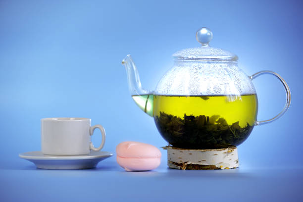 Green tea in a teapot with air marshmallows and a cup on a blue background