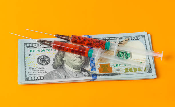 istock Syringes and money on orange background 1207563919
