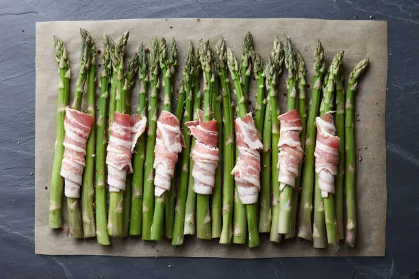 Raw green asparagus wrapped with bacon ready for baking, top view
