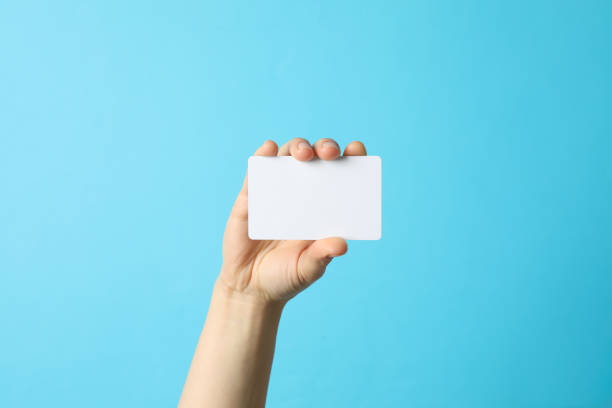 istock Female hand holding empty business card on blue background 1207565704