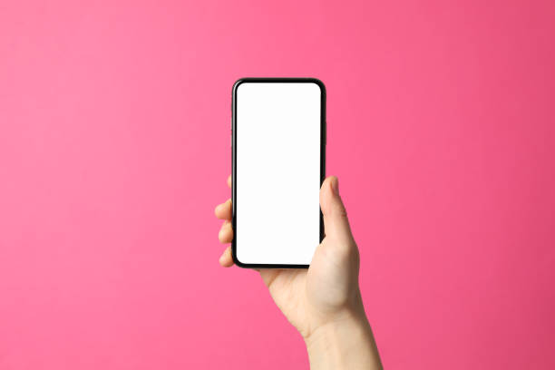 istock Female hand holds phone on pink background. Empty screen 1207566507