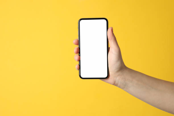 istock Female hand holding phone with empty screen on yellow background 1207566835