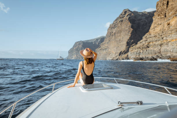 Woman sailing on the yacht near the rocky coast Woman enjoying ocean voyage sitting back on the yacht nose while sailing near the breathtaking rocky coast on a sunset tenerife stock pictures, royalty-free photos & images