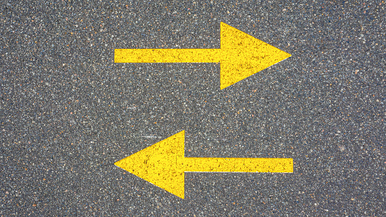 Concept, different directions, two horizontal yellow arrows on asphalt pointing in different directions.