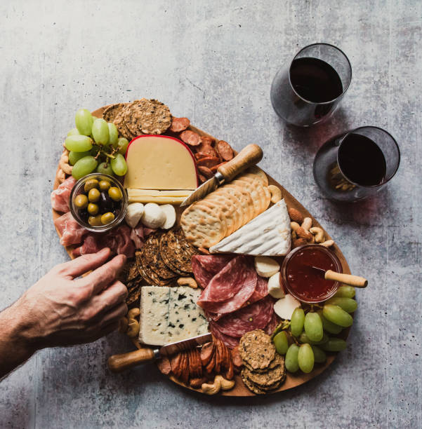 Top view of hand taking food off charcuterie board on stone counter. Top view of hand taking food off charcuterie board on stone counter. in Kingston, ON, Canada prosciutto brie stock pictures, royalty-free photos & images