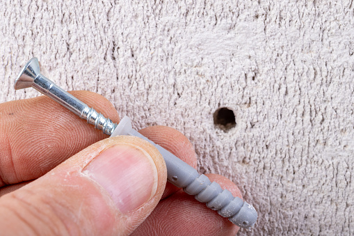 Hole in the wall, screw and dowel for fixing in concrete. Wall mounting methods. Light background.