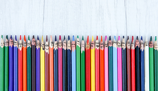 brushes in a row with faces and funny grimace over white wooden background, top view, above