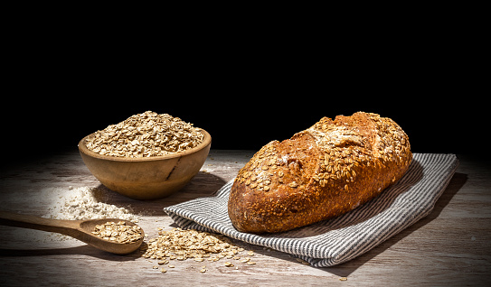 Bread still life with black background. Oatmeal bread with wooden bowl, linen sack, flour and oatmeal on rustic old wood