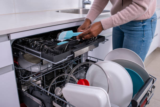 Woman unloading dishwasher after washing. Close up image of a woman's hands holding a spatula, taking out clean cutlery from the dishwasher rack. dishwasher stock pictures, royalty-free photos & images
