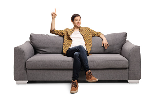 Young man sitting on a sofa and pointing up isolated on white background
