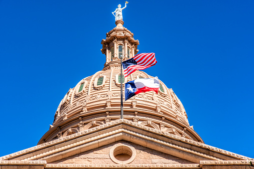 The dome atop the Texas State Capitol Building with the flags of the United States of America and the great State of Texas waving in the foreground.