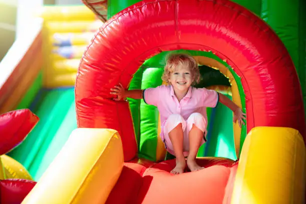 Child jumping on colorful playground trampoline. Kids jump in inflatable bounce castle on kindergarten birthday party Activity and play center for young child. Little boy playing outdoors in summer.