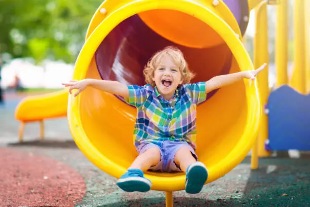 Child playing on outdoor playground. Kids play on school or kindergarten yard. Active kid on colorful slide and swing. Healthy summer activity for children. Little boy climbing outdoors.