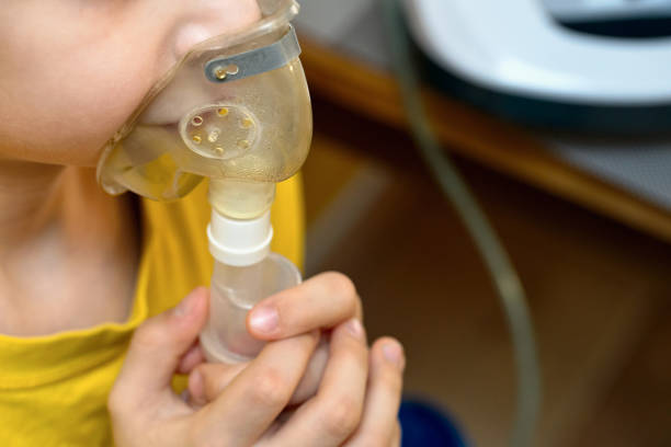 Child makes inhalation at home with nebulizer on out of focus background. Example of combating respiratory diseases such as tracheitis bronchitis pneumonia with medical equipment at home conditions. Child makes inhalation at home with nebulizer on out of focus background. Example of combating respiratory diseases such as tracheitis bronchitis pneumonia with medical equipment at home conditions respiratory disease stock pictures, royalty-free photos & images