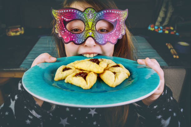 la fille juive dans le masque de carnaval mord le pâté avec des biscuits de purim. - pourim photos et images de collection
