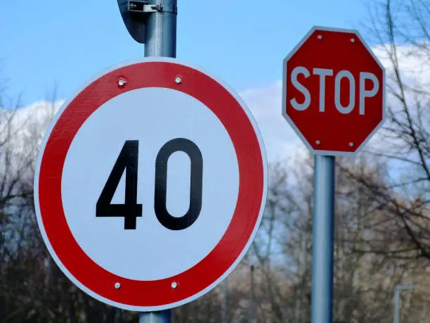 White circular road and traffic sign with red border and the number of 40 limiting and maximizing speed. light blue sky and white clouds above. street scene with bare tree branches in the background.