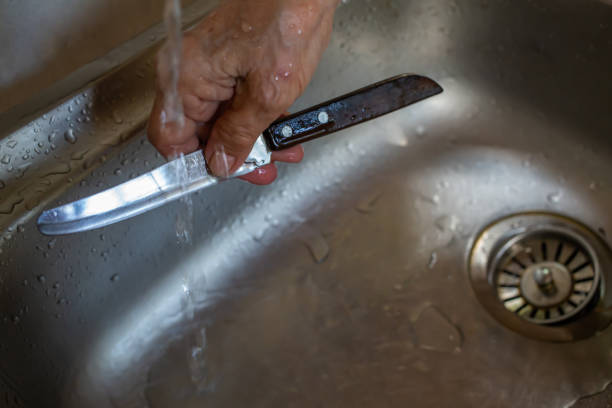 starszy kobieta prawej strony czyszczenia noża w tle zlewu, bliska strzał, selektywne skupienie, kuchnia gotowania koncepcji - cleaning stainless steel steel domestic kitchen zdjęcia i obrazy z banku zdjęć