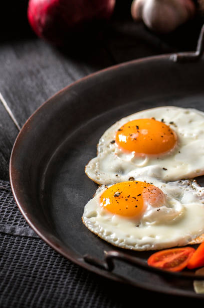 istock Close-up of sunny side up eggs with vegetables on dark background 1207667596
