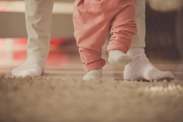 Mother helping her baby daughter walk around her nursery Lower section of unrecognizable mother assisting and holding her baby girl while she takes her first steps around the nursery. first steps stock pictures, royalty-free photos & images
