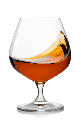 splash of brandy in snifter glass isolated on white background