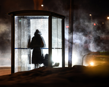 Unidentified woman silhouetted at bus stop on foggy and cold morning