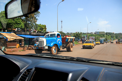 Conakry, Guinea - October 10th 2012: Typical traffic in Conakry. An old blue truck slowing down the following yellow cars. Picture taken from inside a car driving in the opposite direction.