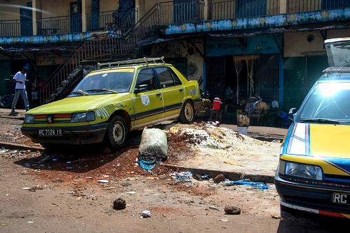 Conakry, Guinea - October 10th 2012: The roadside of Conakry's main street misused as a garbage dump. On top of the dump, the local people have parked cars.