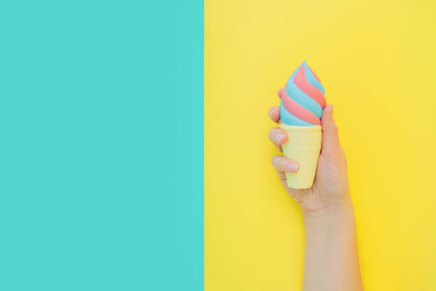 Flat lay antistress toy squish ice cream in waffle cone squezzed in hand.Bright blue yellow background.Compressing,soft,squeezable items to relieve stress,problems,anxieties,worries.Summer concept. el helado de calamares de juguete antiestrés plano en cono de gofres escupió en la mano. amarillo brillante background.compressing,soft,os que se pueden apretar para aliviar el estrés,problemas,ansiedades,preocupaciones. concepto de verano