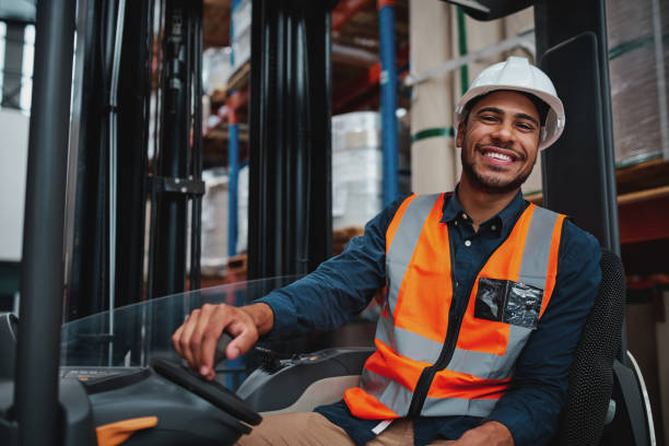 young forklift driver sitting in vehicle in warehouse smiling looking at camera - cargo container imagens e fotografias de stock