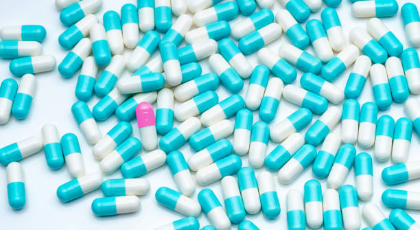 青白カプセルの丸薬の群衆で顕著なピンクホワイトカプセルピル。ユニークで目立つコンセプト。製薬業界。薬局ドラッグストアのコンセプト。抗生物質の薬剤耐性。医療。 - amoxicillin ストックフォトと画像