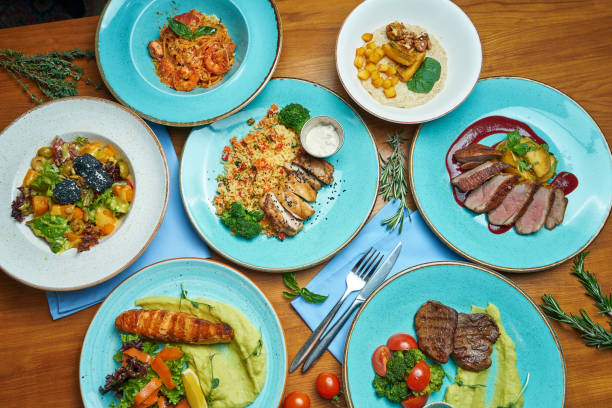 istock Assorted different dishes on a colorful background. Dining table with duck breast, couscous with chicken, steaks, grilled salmon, salads. Top view, food flat lay 1207682767