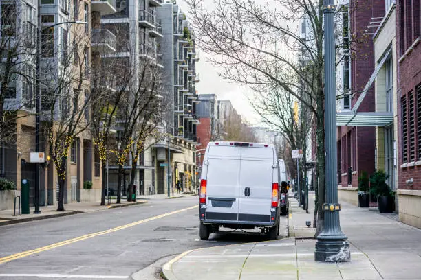 Photo of Compact comfortable industrial cargo delivery mini vans for standing on the city street with multilevel apartments buildings