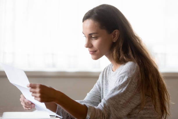 Young woman sit at table reading post letter at home Concentrated millennial woman sit at table at home reading good news in paperwork mail letter, happy young female receive positive answer or decision in post correspondence, consider postal notice college acceptance letter stock pictures, royalty-free photos & images