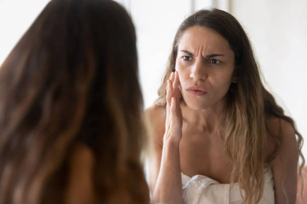 istock Anxious young woman look in mirror worry about skin problems 1207696920