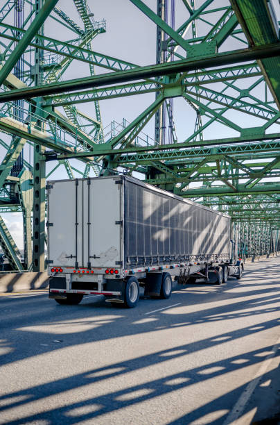 istock Professional industrial diesel big rig semi truck transporting cargo in covered black frame semi trailer running on the truss bascule Interstate Bridge 1207698094