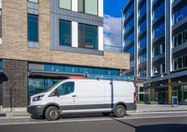 Photo of Commercial compact mini van for small business and deliveries standing on urban city street with multilevel apartments buildings