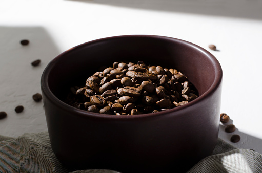 Preparing morning coffee.Clay bowl full of coffee beans, napkin on the white kithcen table