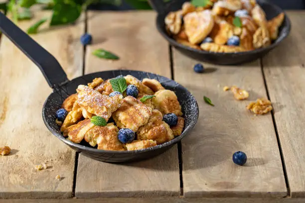 Portion of Kaiserschmarrn in an iron pan with blueberries on a wooden table in the mountains
