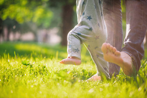 il bambino è felice dei suoi primi passi sostenuti dal padre su un prato estivo - scalzo foto e immagini stock