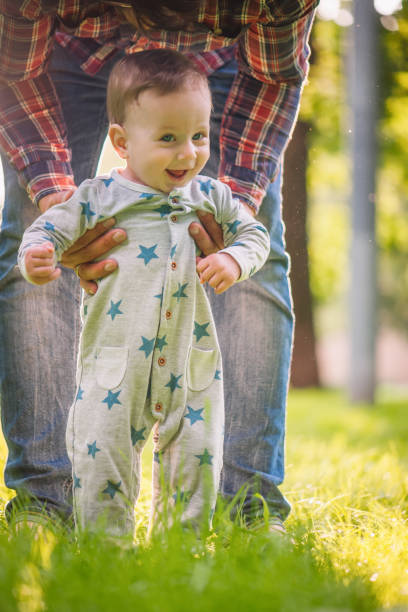 istock Baby boy is happy with his first steps supported by his father on a summer meadow 1207710813