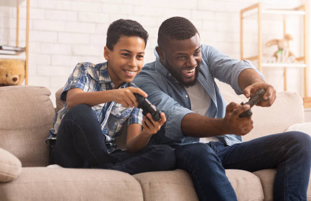 wesoły czarny chłopiec rywalizujący w grach wideo z ojcem - video game friendship teenager togetherness zdjęcia i obrazy z banku zdjęć