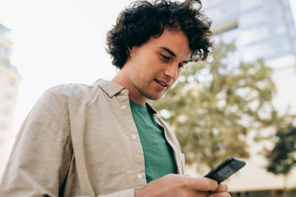 istock Caucasian smart young man standing outdoors, typing messages on mobile phone. Young handsome male with curly hair browsing online on his smart phone in the city street. 1207715201