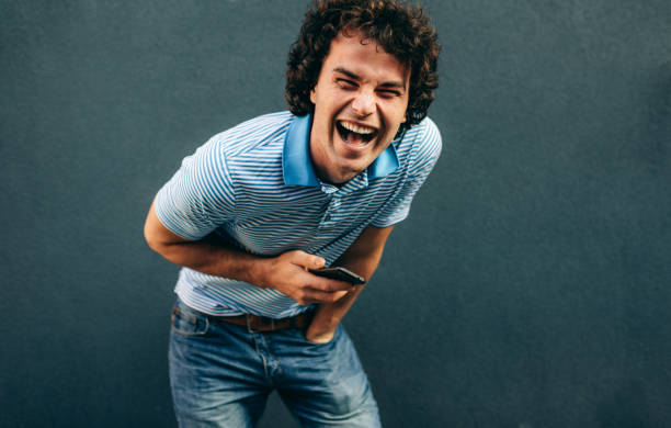 istock Image of cheerful young man posing for advertisement, smiling and looking at the camera, standing at building concrete wall outdoors. Portrait of happy student male posing outside. People and emotion 1207716556