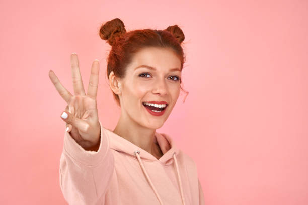Photo of wavy curly charming Caucasian young redhead woman smiling toothily showing you three fingers isolated over pink studio background. Counting gesture. Body language and nonverbal communication Photo of wavy curly charming Caucasian young redhead woman smiling toothily showing you three fingers isolated over pink studio background. Counting gesture. Body language and nonverbal communication. number 3 photos stock pictures, royalty-free photos & images