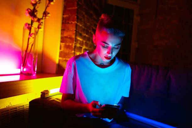 Cinematic portrait of handsome young woman in neon lighted interior Night call. Cinematic portrait of stylish woman in neon lighted interior. Toned like cinema effects, bright neoned colors. Caucasian model using smartphone in colorful lights indoors. Youth culture. teal photos stock pictures, royalty-free photos & images