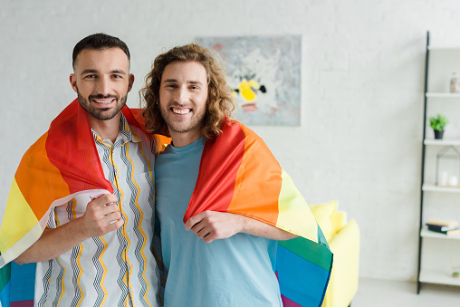 happy homosexual men holding lgbt flag and looking at camera