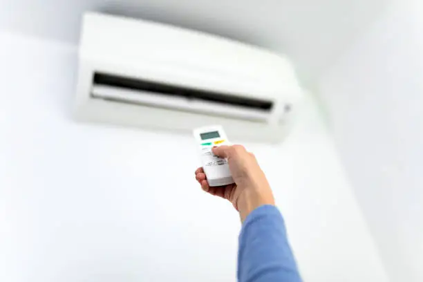 Woman holding a remote of a modern airconditioner unit at home.
